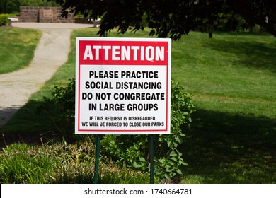 A Park Sign Warning Park-goers To Adhere To The Social Distancing Guidelines Put In Place By The CDC As A Result Of The Covid-19 Pandemic.