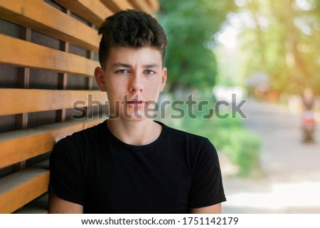 In the park in the summer, a teenage boy tunes in before jogging and meeting with friends. The guy has a beautiful focused face. The guy is not smiling at not wanting to show braces on teeth