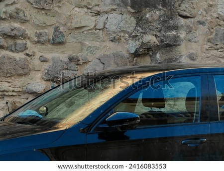 Parked car, against stone wall background. Sun reflection on the windshield. Golden glow color.