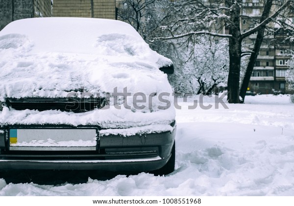 Parked car covered with snow - snow storm, car after\
a heavy snowfall, a lot of snow on the car, car in the snowy yard,\
front view