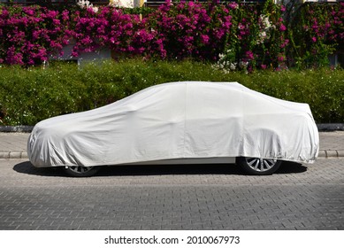 A Parked Car Covered With A Sun Protection Fabric On The Street Of Green City