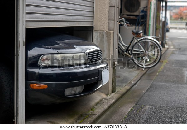 The parked\
car exceeds the size of a garage in the house, Kyoto, Japan. The\
car is parked in a small garage in the city center. Front of the\
car sticking under the door of the\
garage.