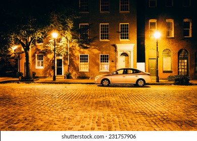 Parked car in front of brick buildings on a cobblestone street at night in Fells Point, Baltimore, Maryland.
