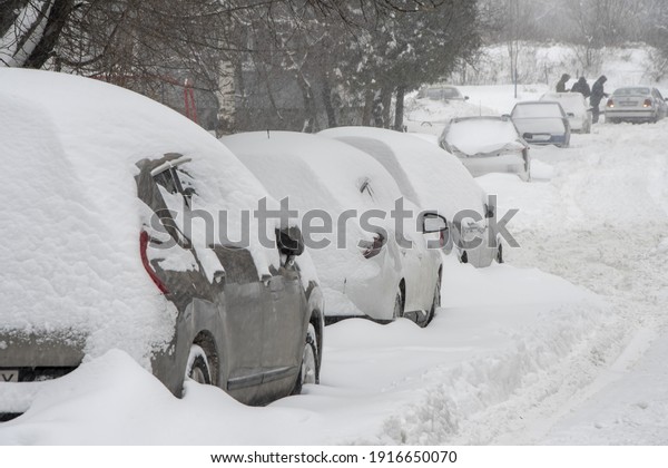 Parked cars are covered in snow, selective focus.\
Snowfall in the city, falling snowflakes. Concept: traffic\
collapse, replacement of summer tires with winter tires, increased\
precipitation and snow 