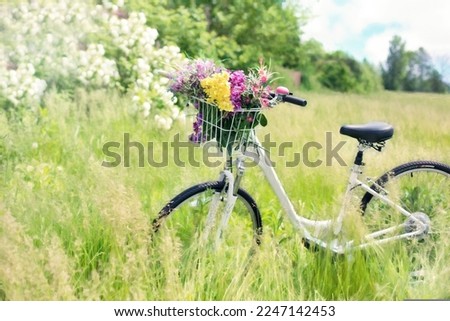 Parked cycle in grass field with flowers in the cage. Looks amazing with the greenery and white flowers in the background.