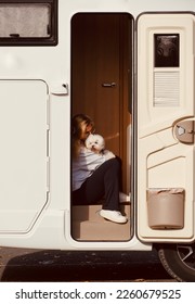 Parked motorhome.Young woman sitting and relaxing at the door of her motorhome with her white bichon maltese dog.Best concept of friends and friendship.Enjoying outdoor leisure activity and lifestyle. - Shutterstock ID 2260679525