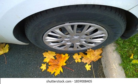 Parked old car wheel. Close up. Yellow fallen maple leaves on asphalt. Golden autumn street. Travelling concept. Driving. Automobile hubcap. Tire pressure.