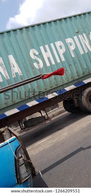Parked shipping truck with car moving past it that\
has a ribbon attached to\
it
