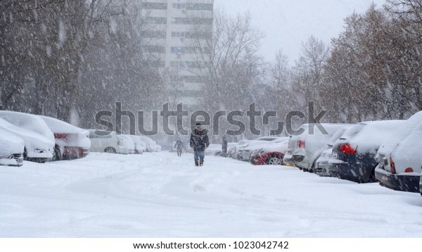 Parking Lot Covered In Snow, People Struggling\
To Walk, Heavy Snowing,\
Blizzard