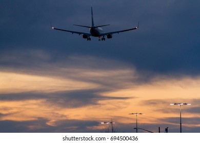 Parking Lot Full Of Cars With Airplane Flying Over At Sunset