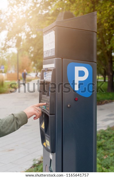 Parking machine in the city street.\
Terminal for paying car parking. Man\'s hand presses\
button.
