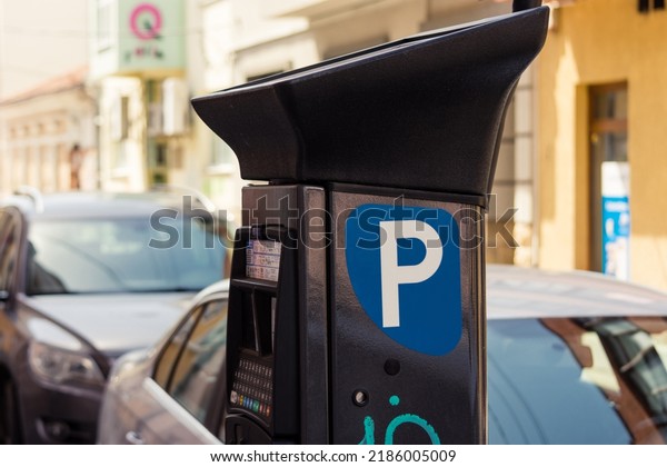 Parking meter next to parked cars on a street\
with old European\
buildings