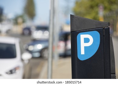 Parking meter or ticket pay station with cars on the road in the blurred background.