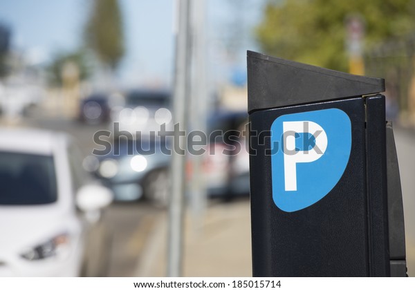 Parking meter or ticket pay station with cars\
on the road in the blurred\
background.