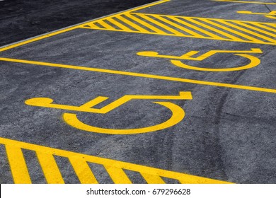 Parking lot with painted yellow sign of wheelchair on asphalt, parking spaces for disabled visitors. Disabled parking spaces.