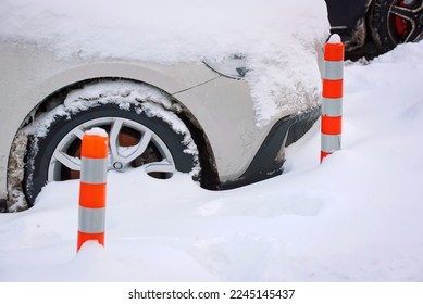 Parking posts placed at snowy parking stall. Car parked close to red bollard. Park post on snowy parking lot. Car wheel stuck in snow. Flexible bollards installed in parking space. 