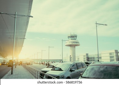 Parking Lot And Road Near Modern Contemporary Airport Terminal In Front Of Air Traffic Control Tower, With Many Passengers And Staff Passing In Distance, Barcelona, Spain