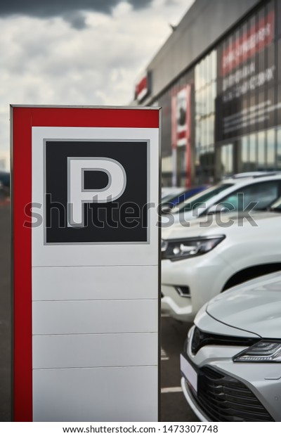 A parking sign at a car dealership close-up and the\
cars behind it.