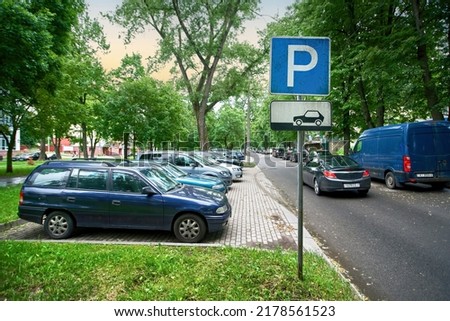 Parking lot sign, cars parked under green trees in residential area, Parking zone. Parking problems not enough free space. Crowded public parking lot on narrow street. Rows of cars parked on roadside
