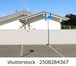 Parking sign in front of two white modern houses with gray plaster fence. Parking lot in front. Background for copy space.