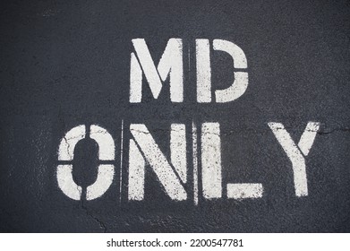 Parking spot reserved for MD. White stenciled lettering on asphalt parking spot. Taken outside a private practice, but could be outside a hospital or urgent care facility.