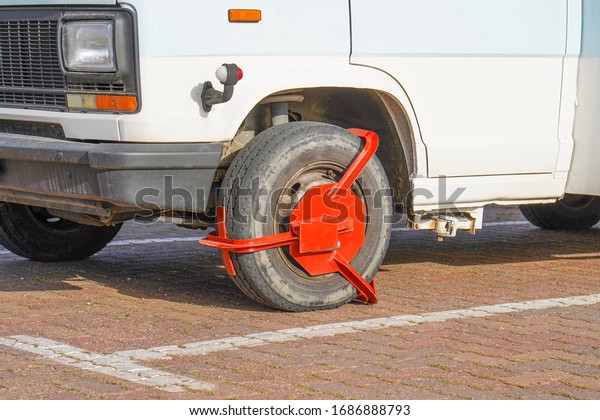 Parking Wheel Lock. Clamped front wheel of\
illegally parked car, red clamp attached to wheel. Car parked\
illegally is fined and wheel-locked by the\
police.