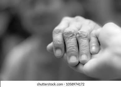 Parkinson And Alzheimer Female Senior Elderly Patient With Caregiver In Hospice Care. Old Woman Holding Hand With Nurse Or Daughter In Black And White.