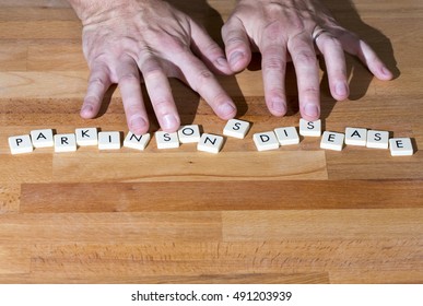Parkinson's disease text on a wooden table. Shaking fingers touches the letters.