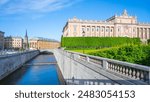 The Parliament House alongside its waterway shines under a clear blue sky on a bright day in Stockholm, Sweden.