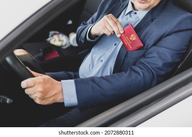 Parliamentary immunity concept. Man in blue suit shows red ID card or pass. An important untouchable employee of ministry is driving a car. state Duma deputy of Russia inscription on the red document.