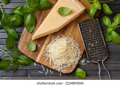 Parmesan cheese with grater on a cutting board. Whole wedge and grated grana padano cheese, stainless steel grater and fresh basil herb on a wooden background. Dairy product. Top view.