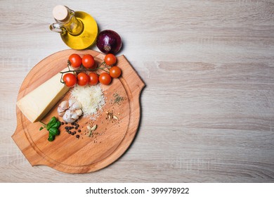 Parmesan cheese on a wooden board and cherry tomatoes, olive oil, onions, garlic, spices.