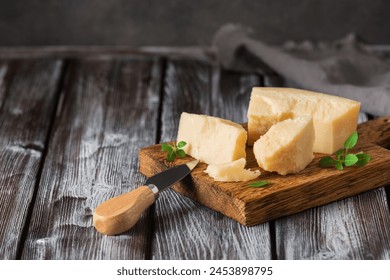 Parmesan cheese pieces on a wooden cutting board, dark wooden background. Side view, selective focus, copy space. - Powered by Shutterstock