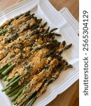 Parmesan crusted asparagus, prepared on a white serving platter, resting on a wooden table. A perfect dinner side dish for any meal. 