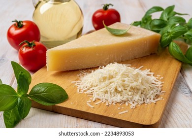 Parmesan and tomatoes on a cutting board. Italian grana padano cheese wedge and grated, red tomatoes, green basil herb and olive oil over white wooden table. Delicious hard cheese. Front view. - Powered by Shutterstock