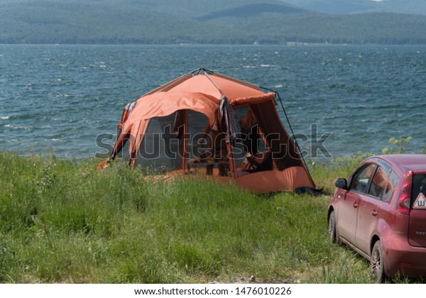 Parnaia,\
Sharypovskiy district, \
Krasnoyarsk region/ RF - 5 July 2019: Red\
gazebo-tent with mosquito net stands next to the crimson car during\
the summer holiday on the shore of the\
lake.