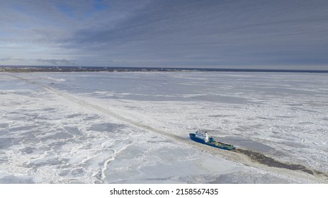 PARNU, ESTONIA - Feb 27, 2022: Aerial View To The Ice Breaker Assisting Cargo Ship To Reach The Harbor Via Waterway Through  The Frozen Sea Bay