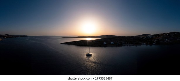 Paros Island, Greece, Panorama Aerial Drone View At Sunset. Sun Falling Over The Calm Aegean Sea, Catamaran Boat Moored At Open Sea, Panorama, Greek Islands Cyclades. Summer Vacations Destination