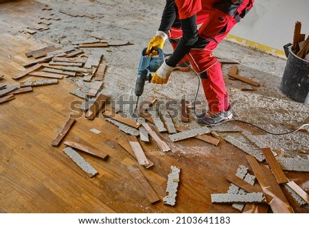 Parquet in wood glued to the slab, removed with an electric demolition hammer by a craftsman in workwear, in the apartment under renovation. In the foreground, the removed parquet slats. 