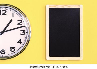Part of analogue plain wall clock and black notice board on trendy yellow background. One o'clock. Close up with copy space, time management or school concept and lunch time opening hours