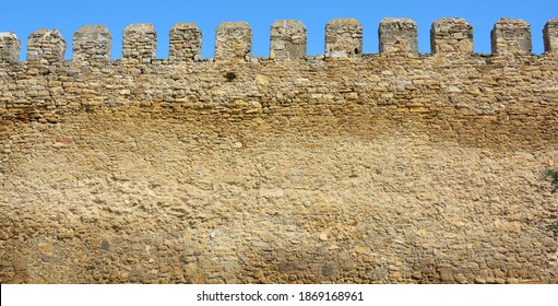 A part of an ancient fortress wall, castle wall with a tooth shaped parapet made from limestone bricks, coquina rocks, yellow shell rocks against the blue sky. 