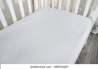 Part Of Baby Cot, Close Up. Mattress And Sheets In White Crib.