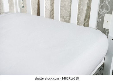 Part Of Baby Cot, Close Up. Mattress And Sheets In White Crib.