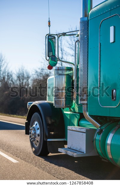 Part of big rig bright\
green classic American semi truck with extended cab for long haul\
routs transporting semi trailer driving on the straight highway in\
sunny day
