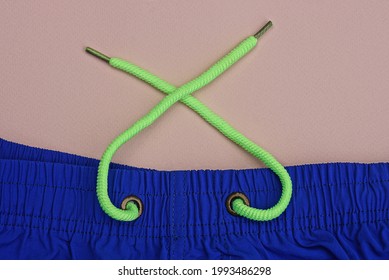 Part Of Blue Fabric Sweatpants With Elastic And Long Green Laces On A Pink Table
