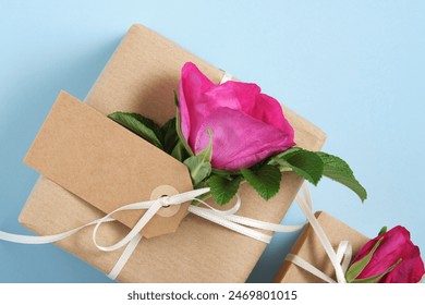 Part of brown gift box with empty label and rosehip flowers on blue background. Space for your text
