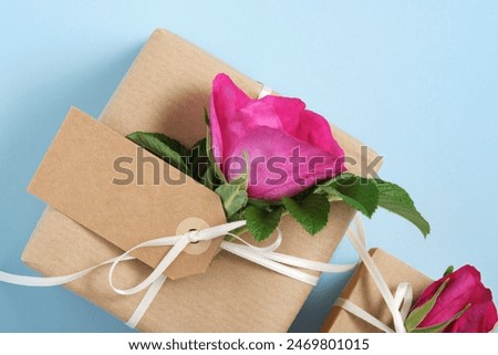 Part of brown gift box with empty label and rosehip flowers on blue background. Space for your text