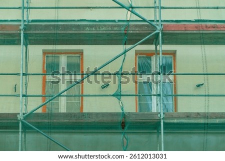 part of the building's facade during renovation work. Scaffolding and green protective netting are visible on the facade. The windows are protected with foil, and their frames have orange frames.