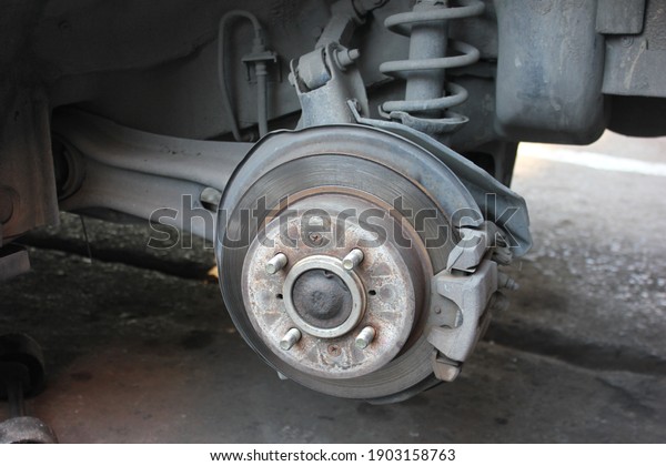 Part of car parking on\
ceramic tile inside a garage with the car waiting for the mechanic\
to change its tires, wheel, tire disc brake, disc brake and shock\
absorber object.