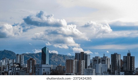 Part of the city of 'Manizales' is seen with a landscape of the mountains in the background and a sky with abundant clouds, but with a shine on the sun's buildings.